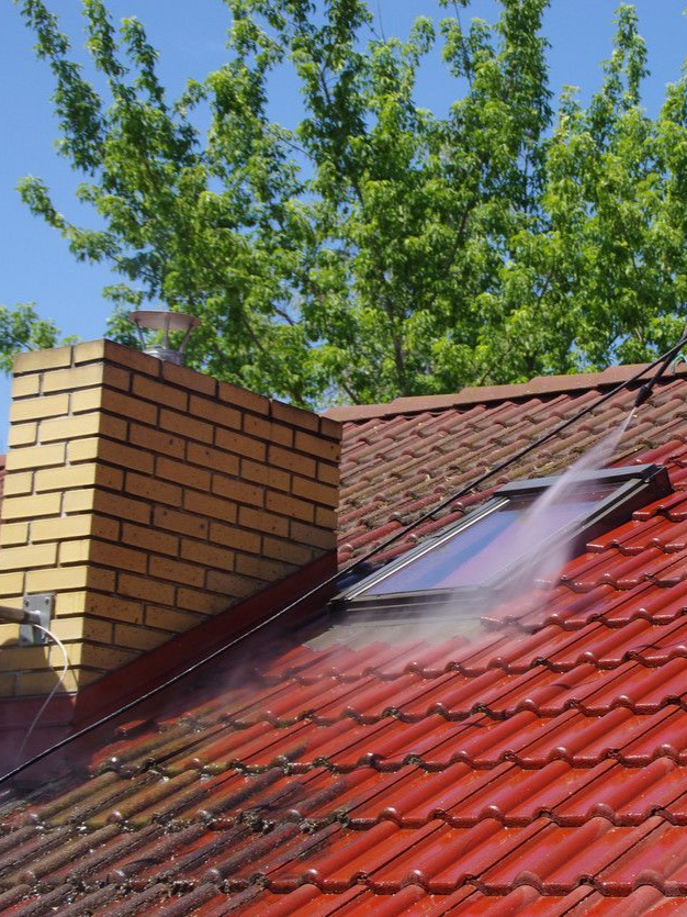 Un toit rouge est nettoyé au nettoyeur haute pression.
