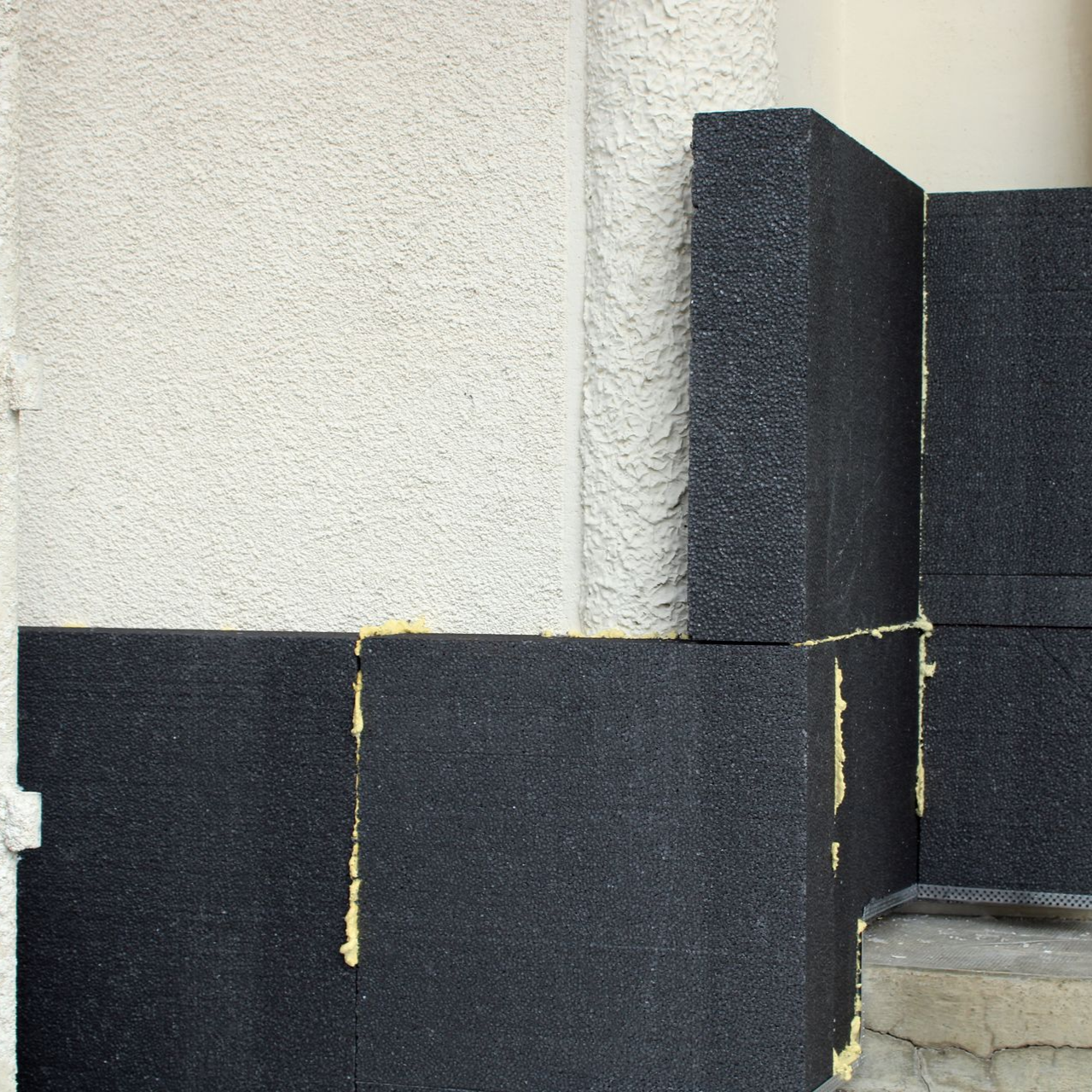 Panneaux d'isolation en mousse foncée appliqués sur un mur extérieur de bâtiment.