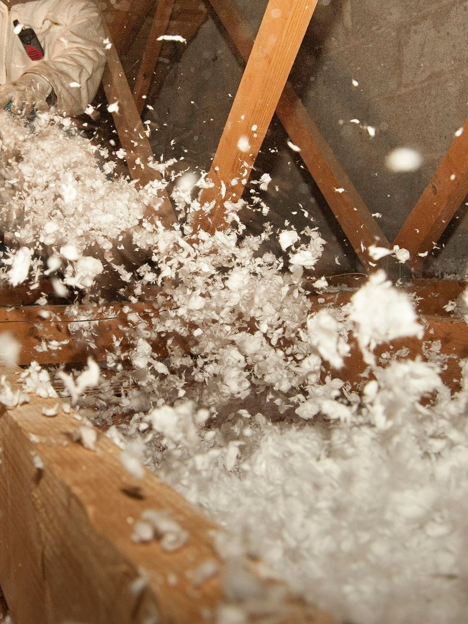 Combles isolés avec un isolant blanc duveteux ; poutres en bois visibles.