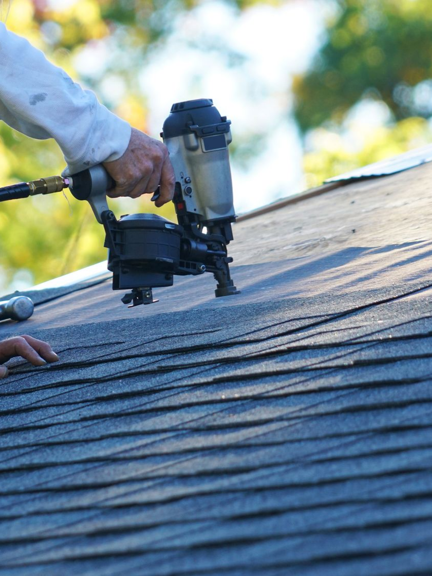 Un couvreur utilise un cloueur pneumatique pour installer des bardeaux d'asphalte sur un toit.