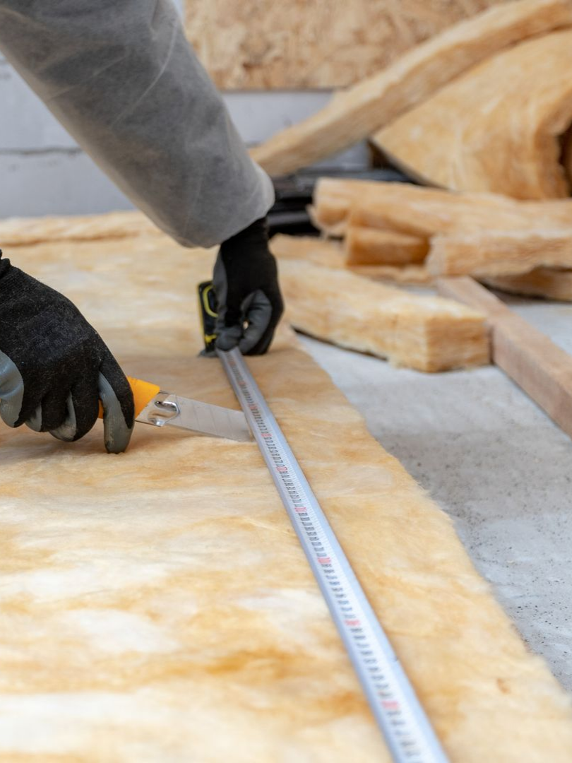 Une personne portant des gants découpe de l'isolant avec un cutter et une règle.