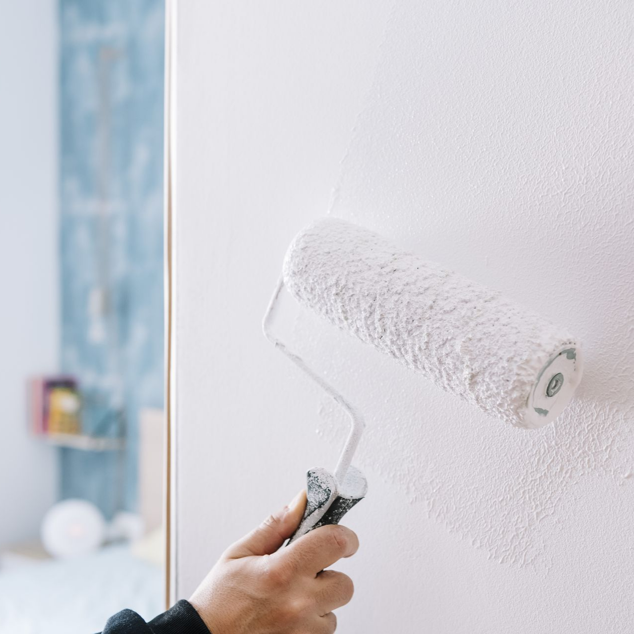 Main utilisant un rouleau à peinture sur un mur blanc.