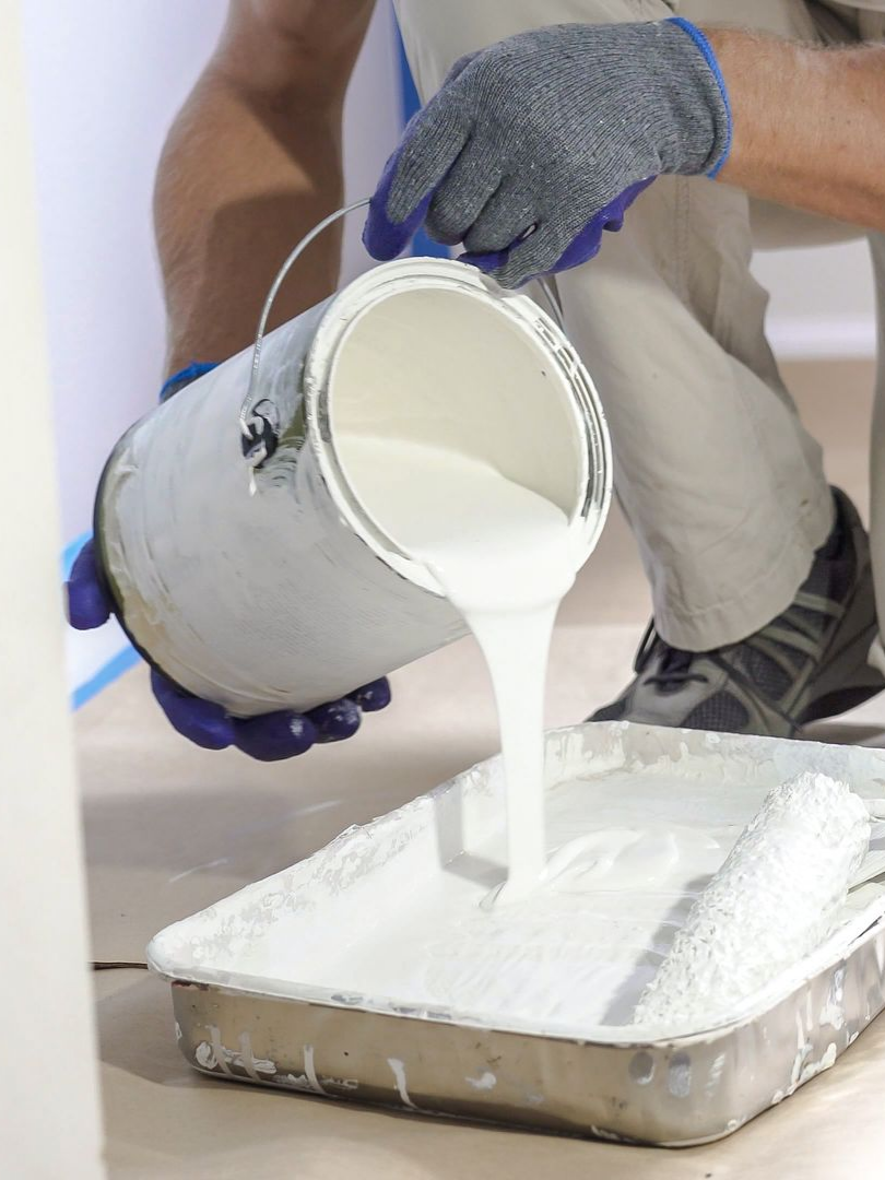 Une personne verse de la peinture blanche d'un pot.