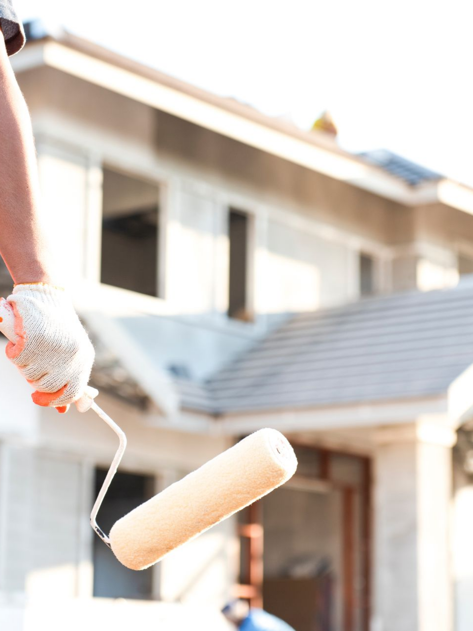 Personne portant des gants utilisant un rouleau à peinture sur l'extérieur d'une maison.