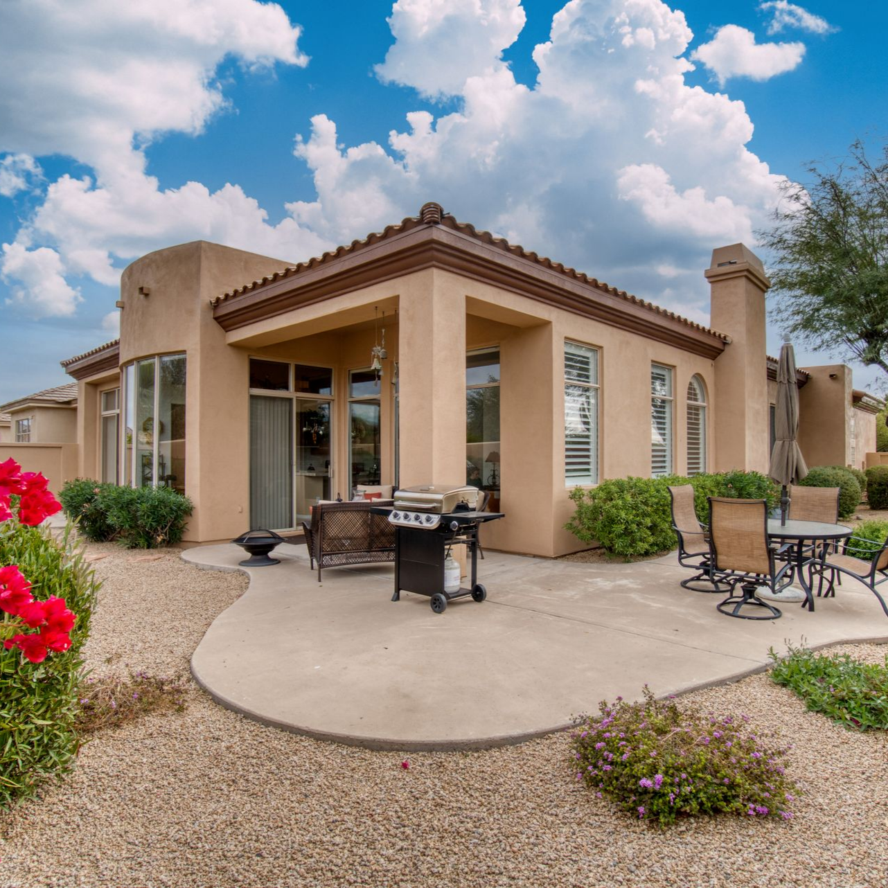 Maison beige avec terrasse, barbecue et mobilier de jardin.