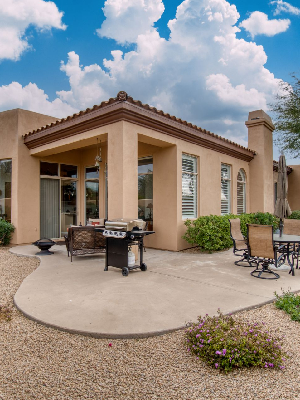 Maison beige avec terrasse, barbecue et mobilier de jardin.