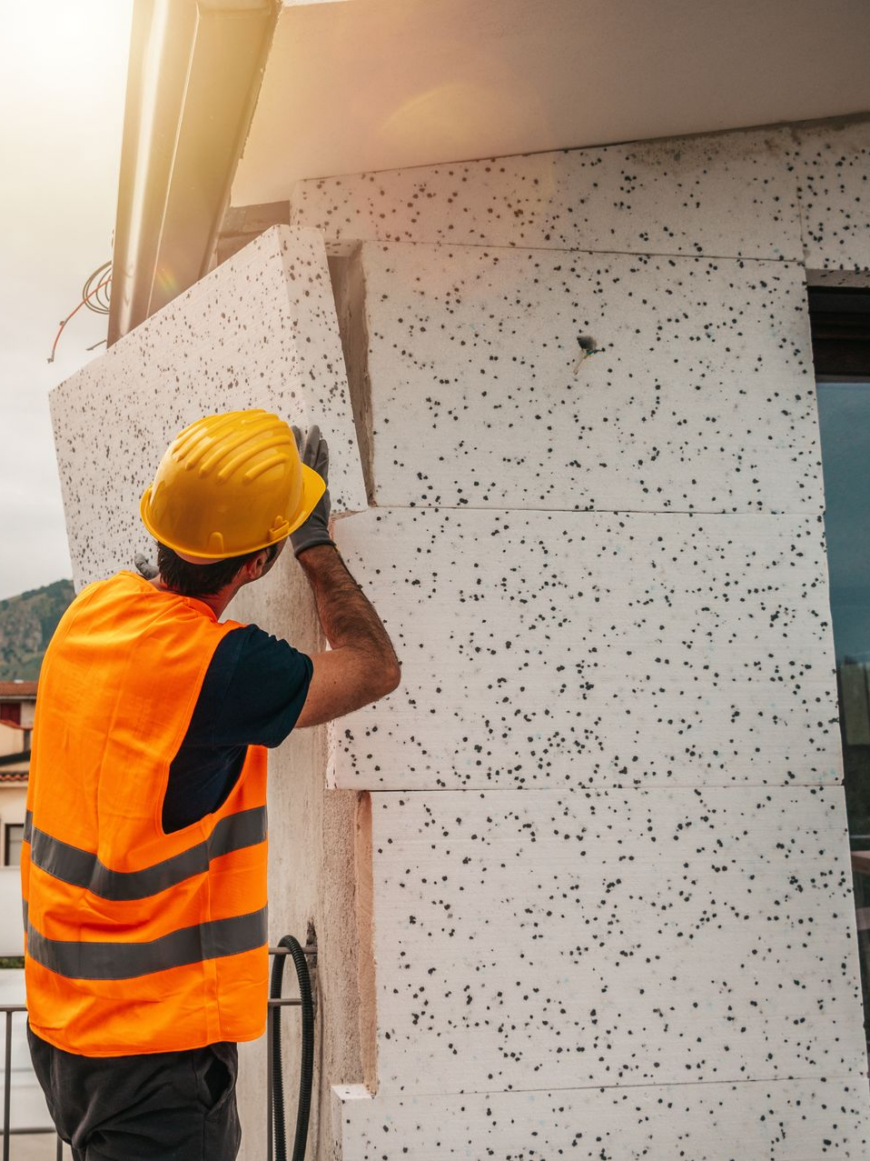 Un ouvrier du bâtiment installe un isolant en mousse sur la façade d'un bâtiment.