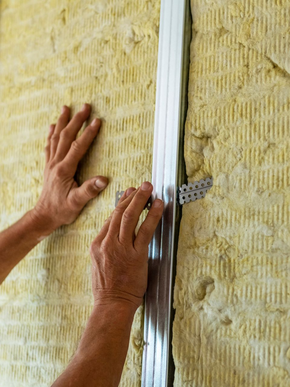 Des mains installent un montant métallique dans un mur isolé.