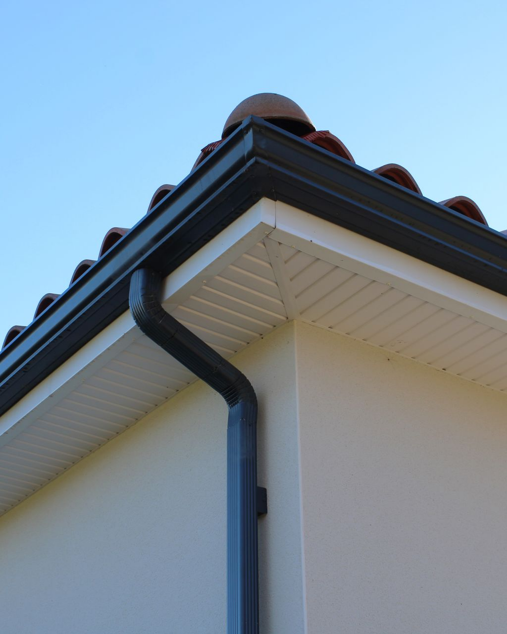 Gouttières noires à l'angle d'une maison blanche.
