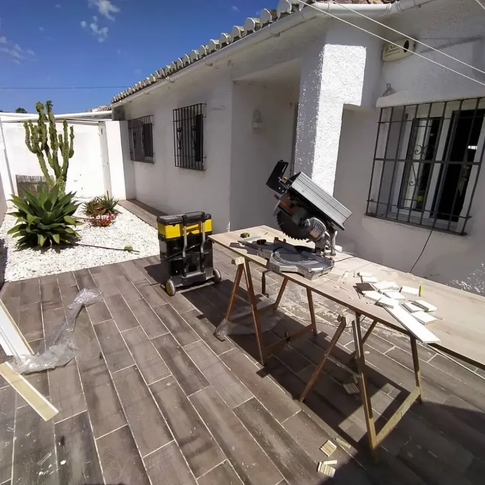Trabajadores pintando una pared exterior y una puerta junto a un sendero en un patio.
