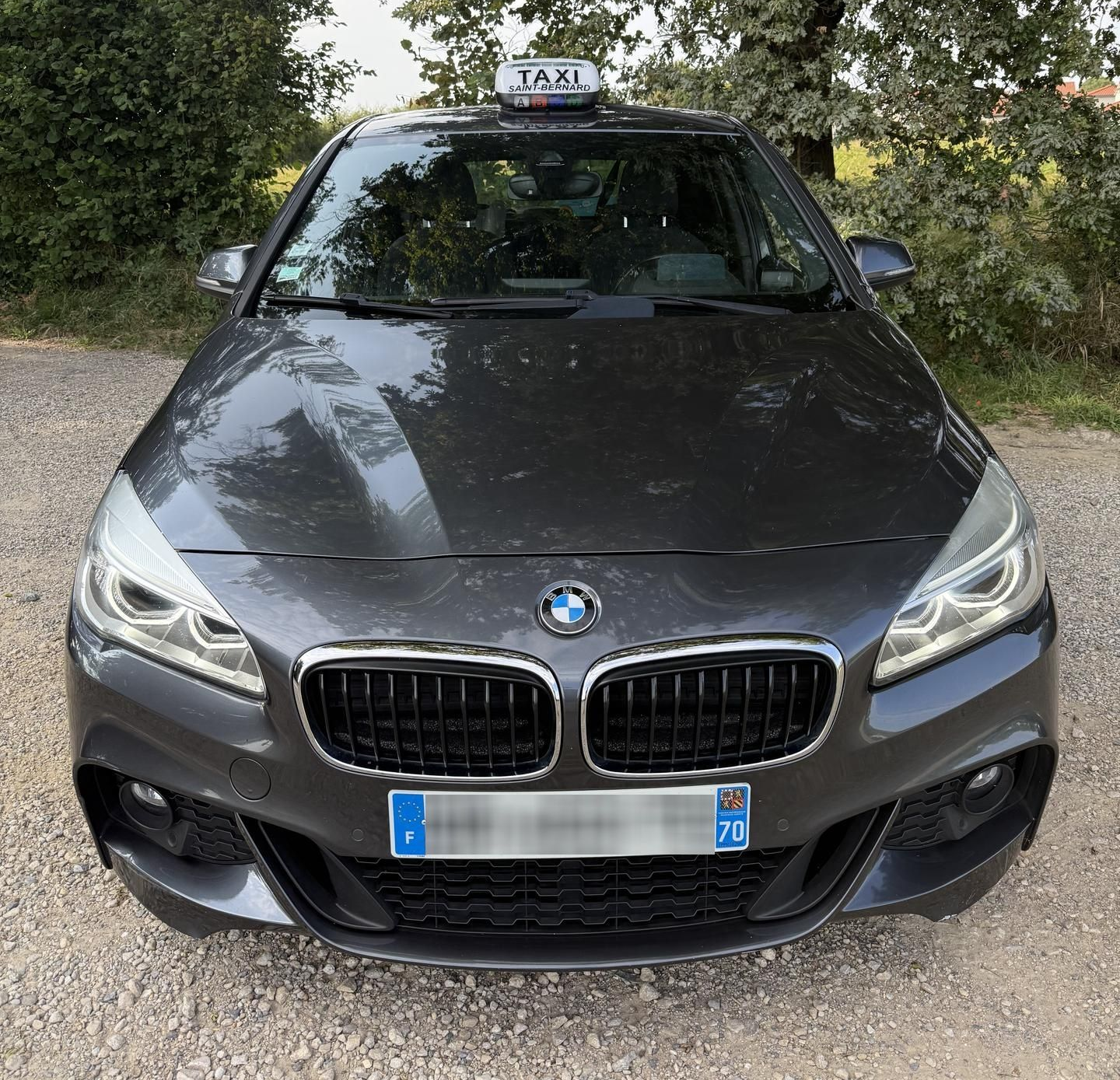 Un taxi BMW gris foncé stationné sur un chemin.