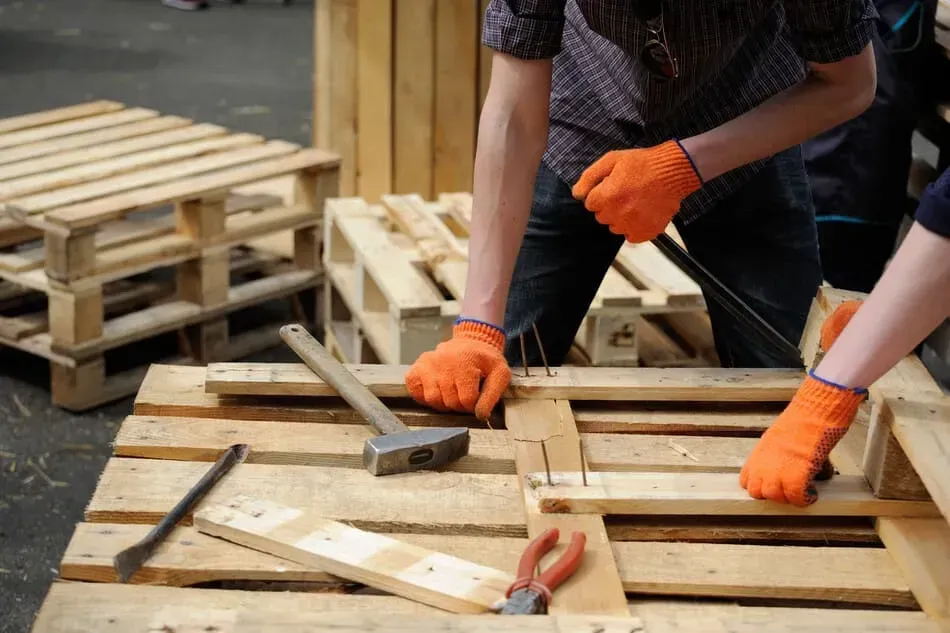Un hombre está trabajando en una paleta de madera con un martillo y alicates.