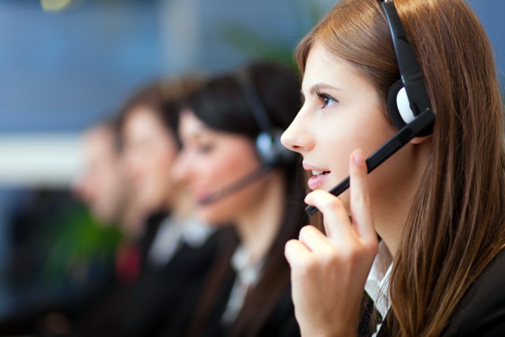 A woman wearing a headset is talking on a cell phone in a call center.