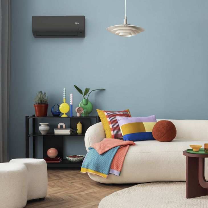 Salon avec mur bleu, canapé blanc avec coussins et couverture colorés, étagère noire et climatiseur