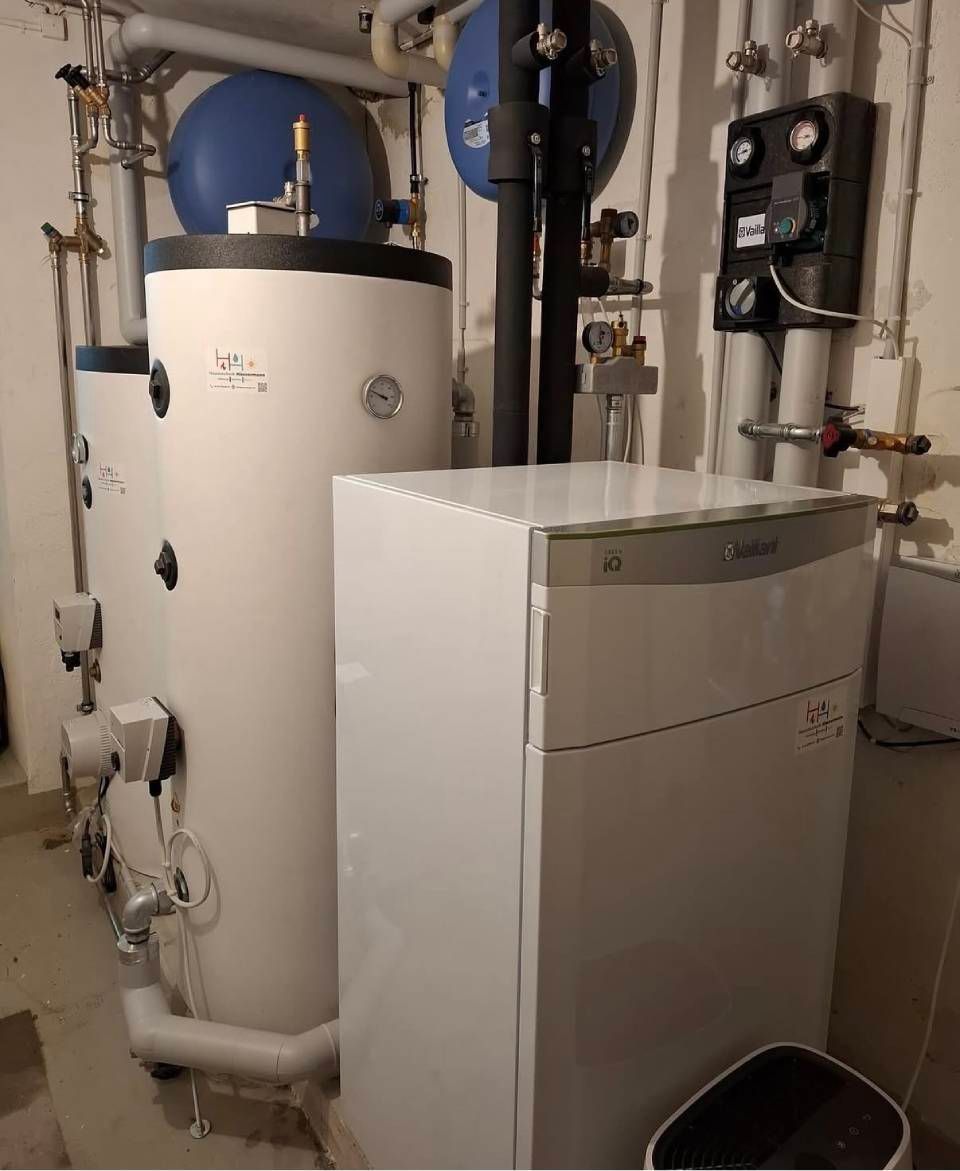 Hauswirtschaftsraum mit einem weissen Warmwasserbereiter und Heizgeräten neben freiliegenden Rohren und Tanks.