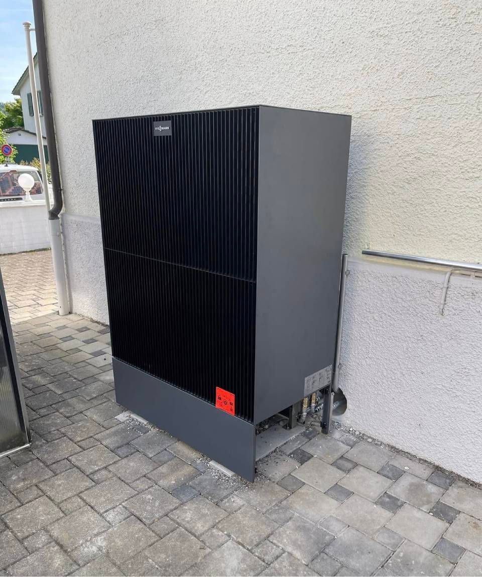 Ein schwarzer Aussenverteilerkasten steht vor einer Stuckwand auf einem gepflasterten Gehweg.