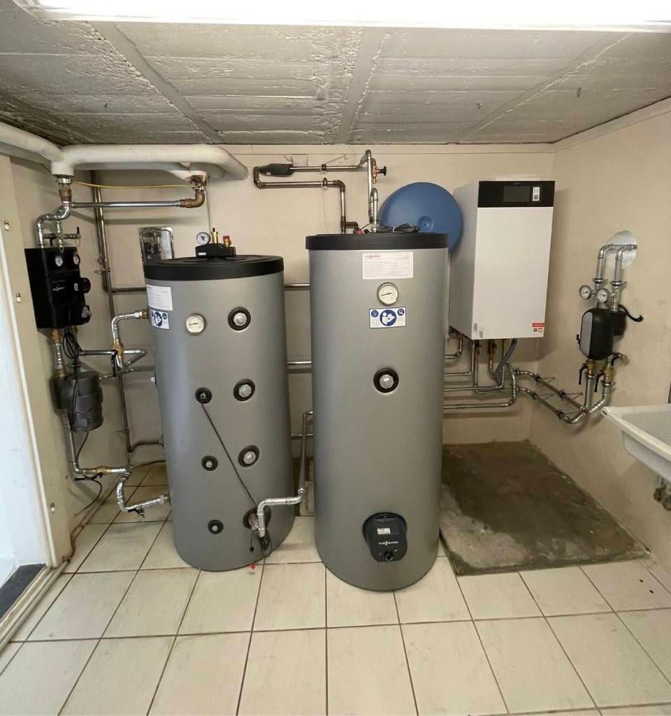 Heizraum mit zwei grossen Grauwassertanks, wandmontierten Geräten, Rohrleitungen und Fliesenboden