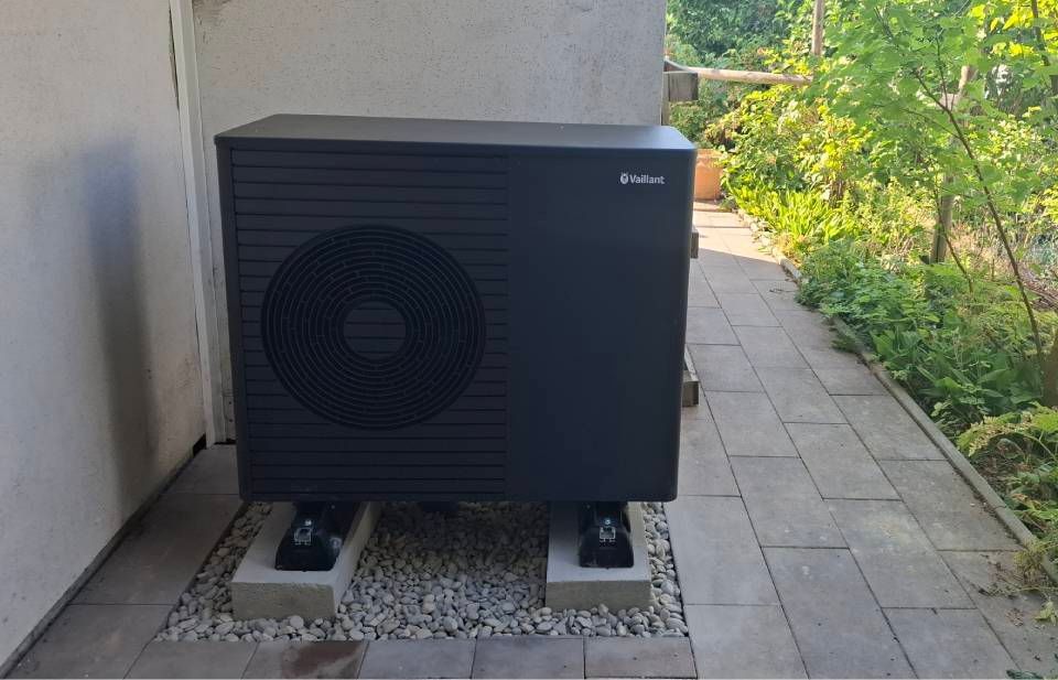 Aussengerät der Wärmepumpe neben einer Hauswand auf einer Kiesfläche neben einem gepflasterten Weg