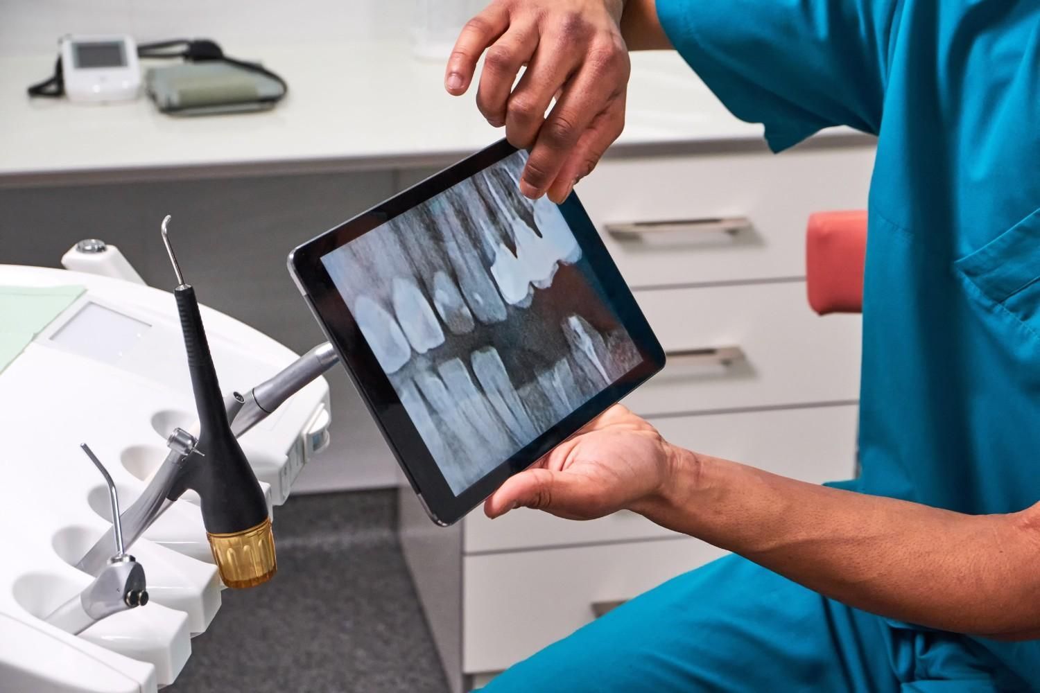 Un dentista sostiene una tableta de rayos X junto a un sillón dental en una clínica.