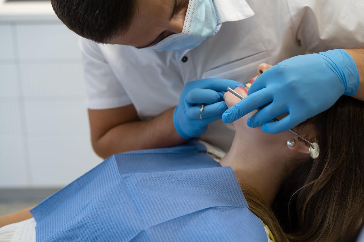 Dentista examinando los dientes de un paciente con las manos enguantadas en el sillón de la clínica.