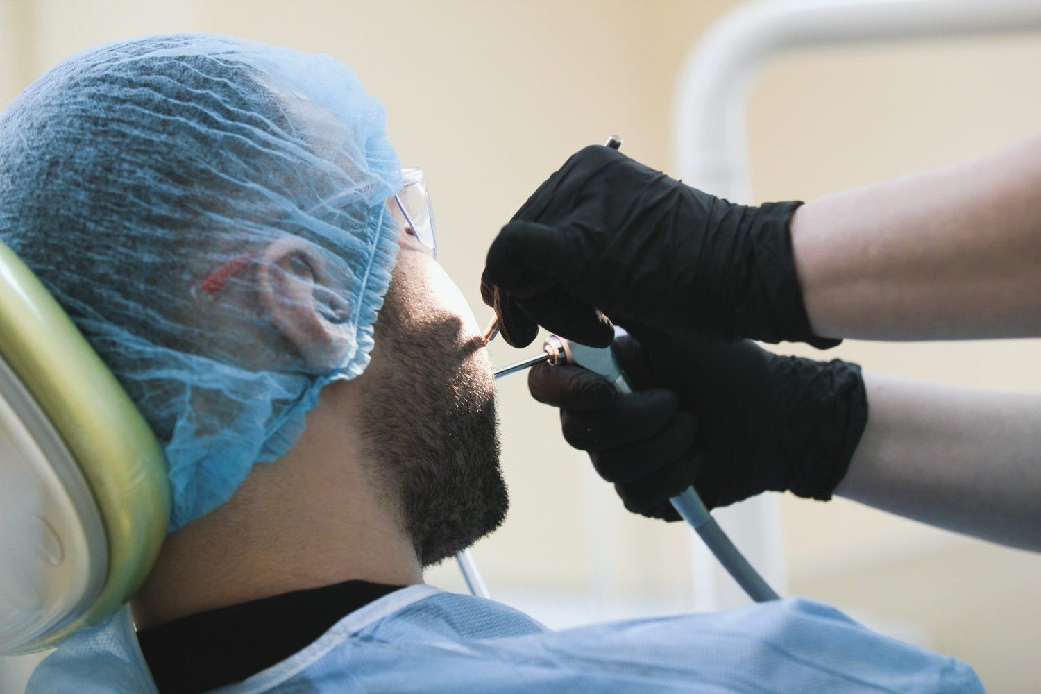 Odontólogo examinando la boca de un paciente con un instrumento mientras el paciente está reclinado en una silla.