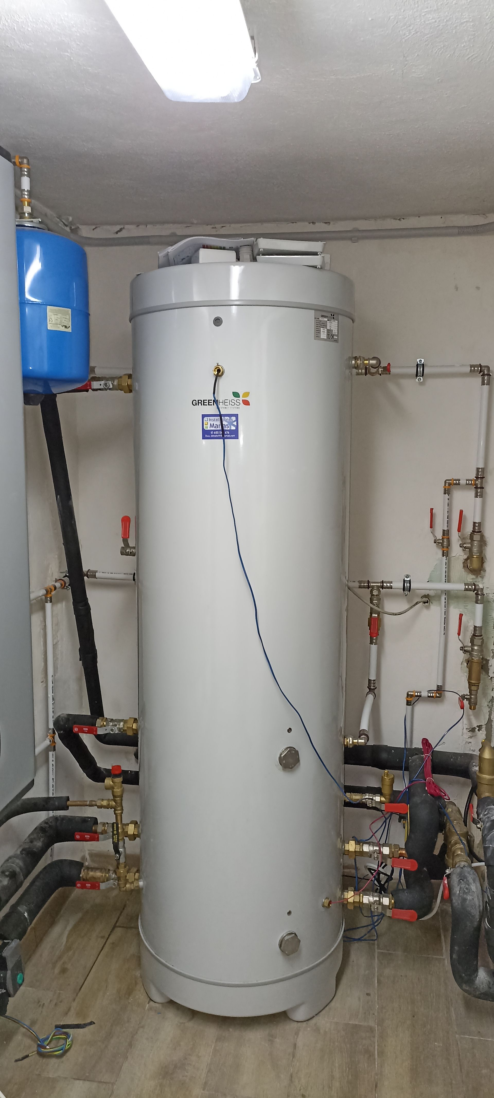 Un gran calentador de agua blanco está en una habitación con tuberías.