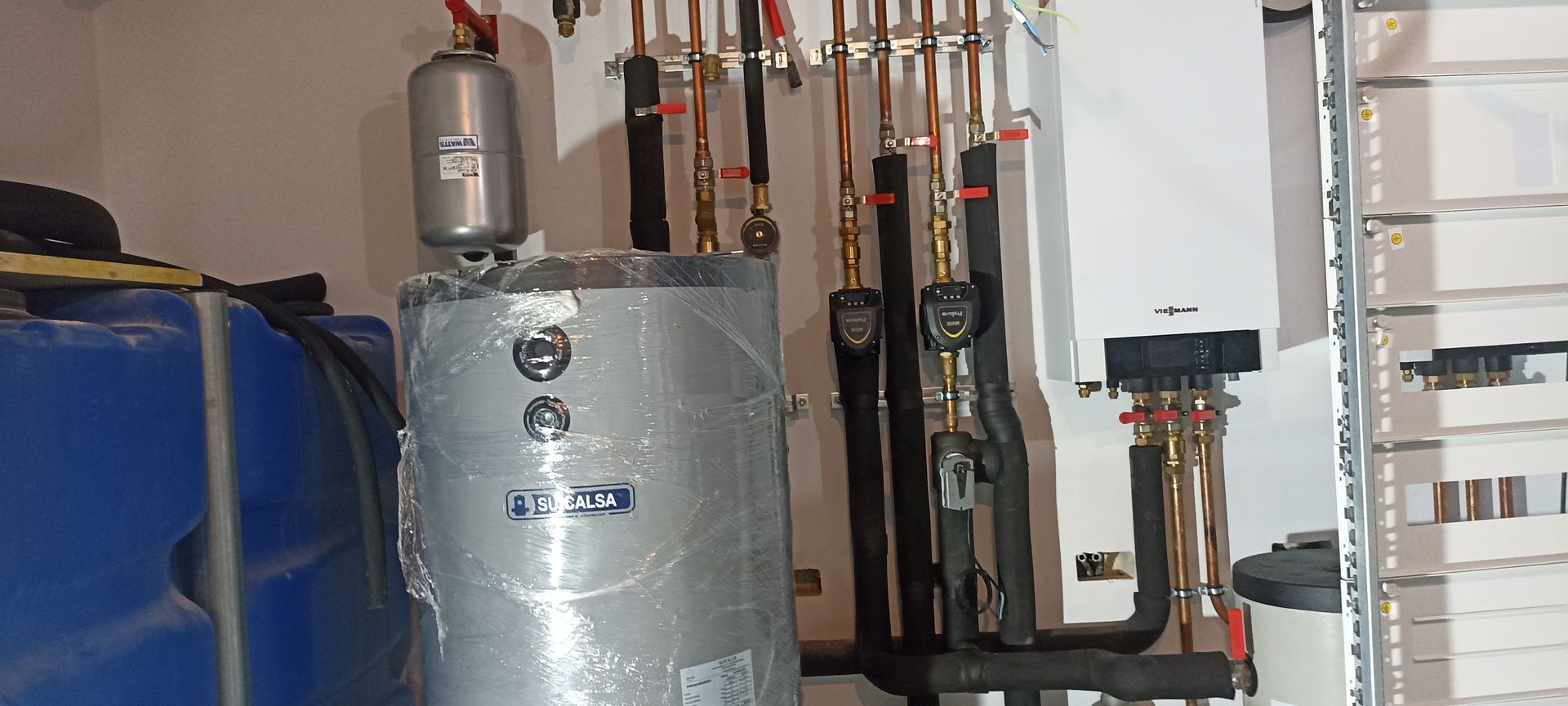 Un calentador de agua está en una habitación al lado de un tanque azul.