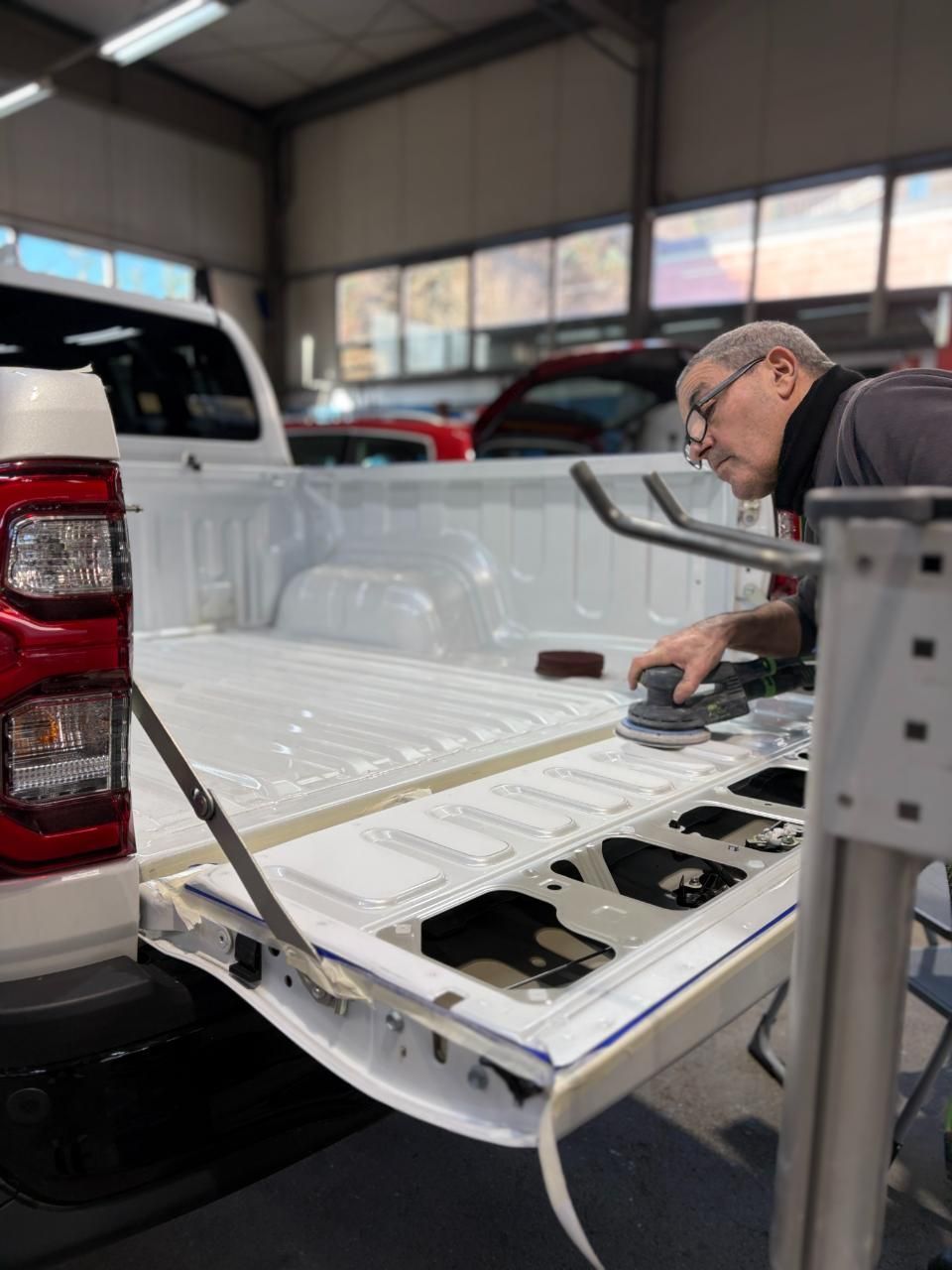 Un uomo ispeziona il portellone posteriore aperto di un pick-up bianco all'interno di un garage.
