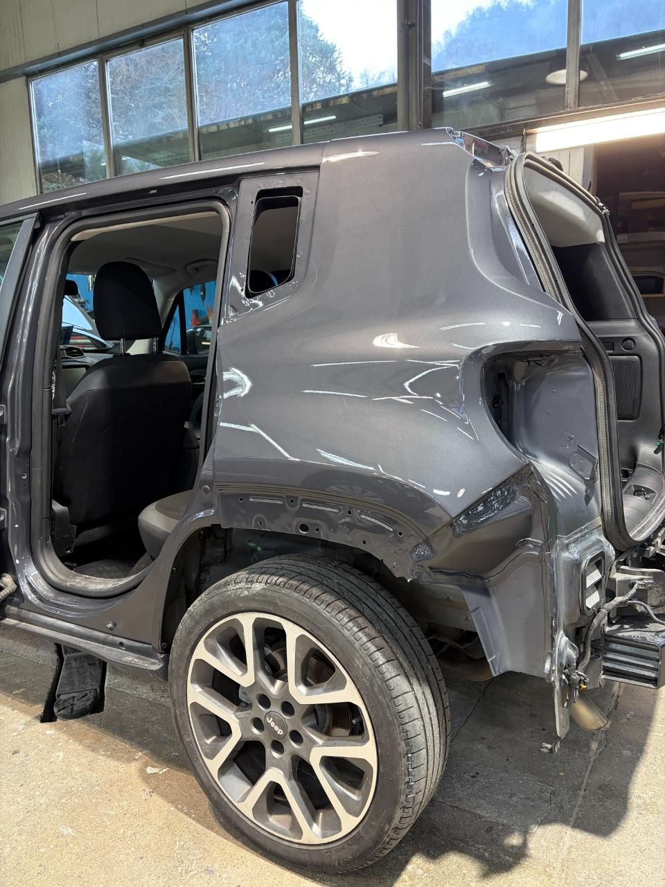 SUV grigio danneggiato con lesioni laterali e posteriori alla carrozzeria, parcheggiato all'interno di un garage con la porta aperta e la ruota posteriore visibile.