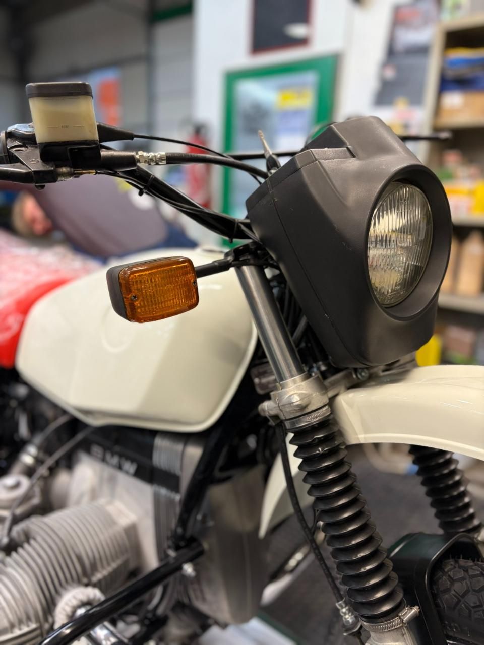 Primo piano di una motocicletta bianca con faro nero e indicatore di direzione ambra in un garage.