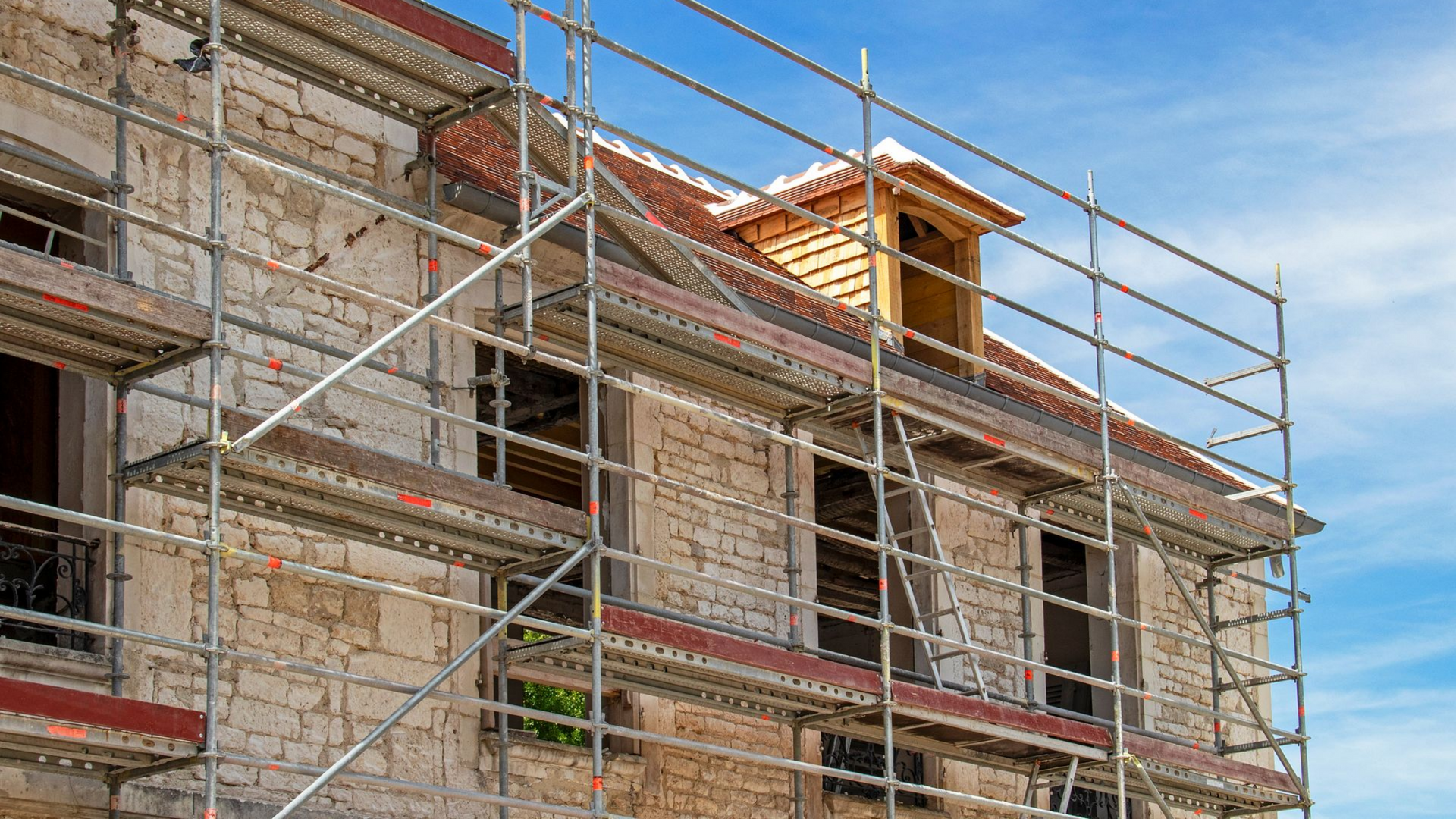 Des échafaudages entourent la façade d'un bâtiment ; des travaux de construction sont en cours sur un extérieur en pierre claire.