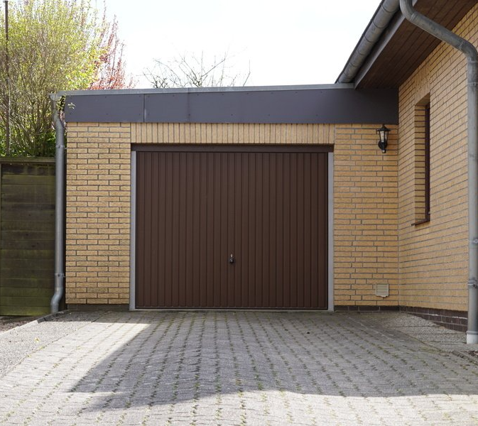 Porte de garage basculante marron sur une maison en brique