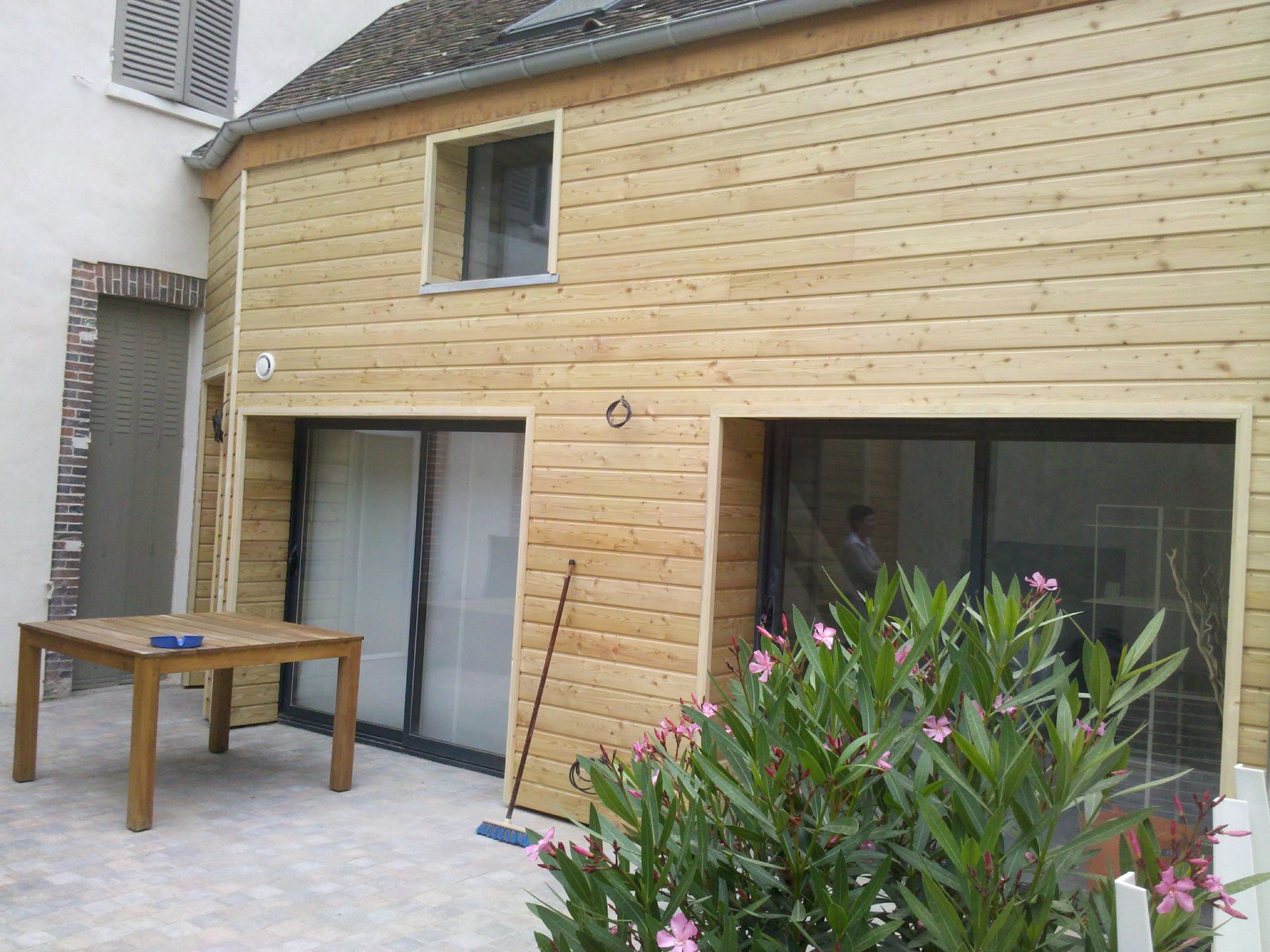 Patio arrière avec terrasse en bois, portes coulissantes vitrées et arbuste fleuri