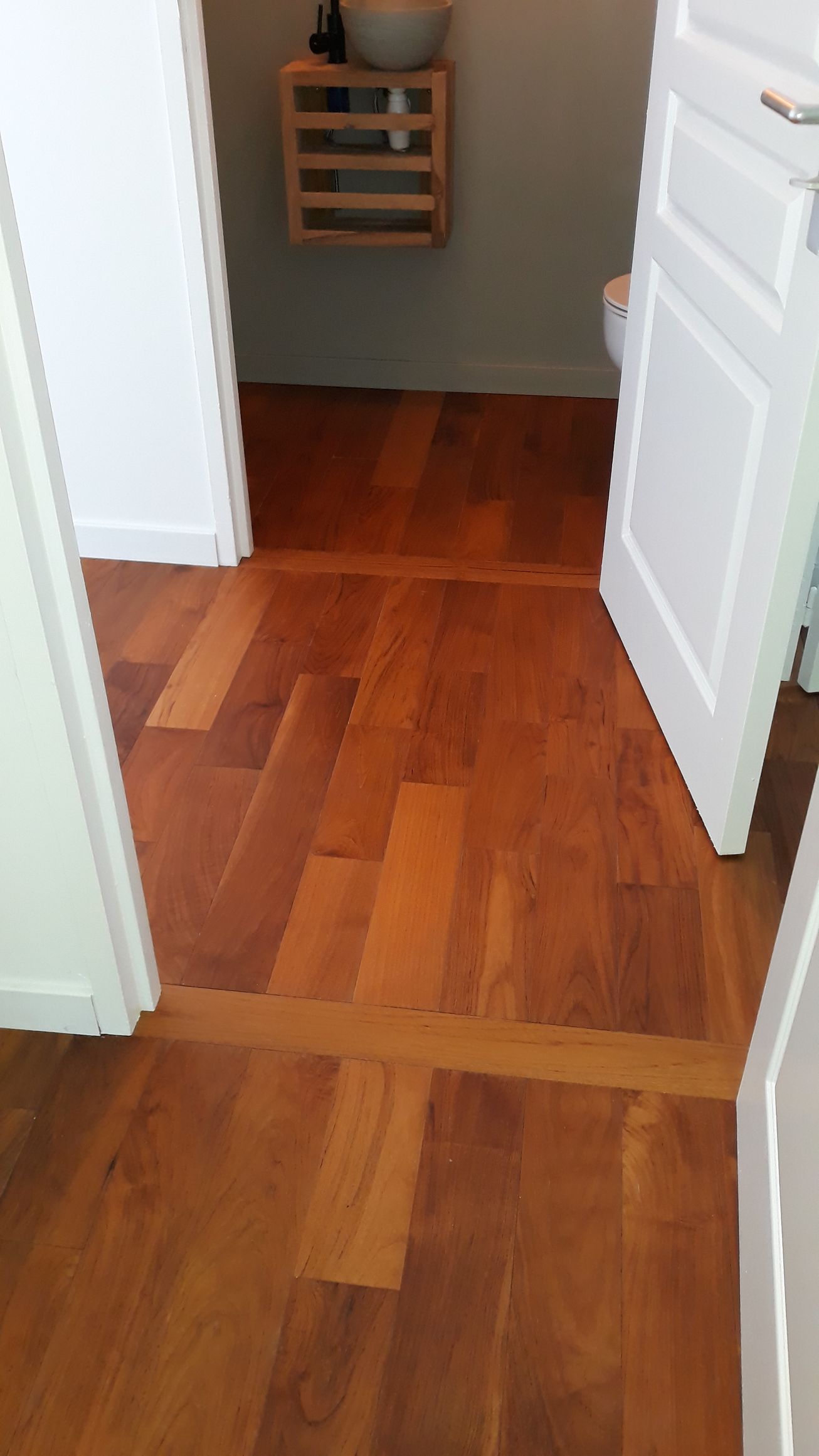 Portes blanches ouvertes encadrant un couloir au parquet chaleureux, avec une petite étagère murale au fond.