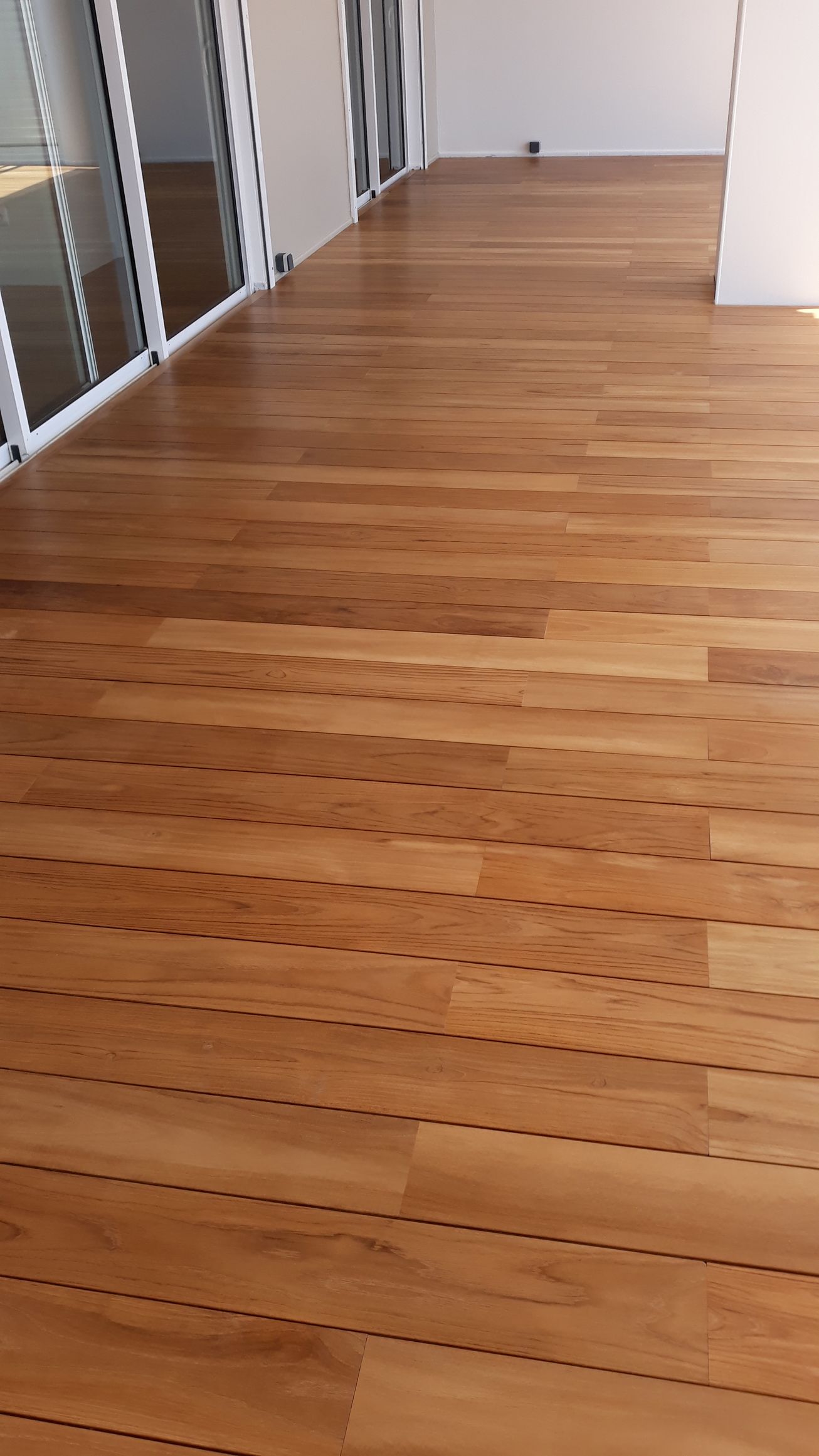 Couloir de bureaux vide avec un sol en bois et des pièces vitrées sur la gauche.