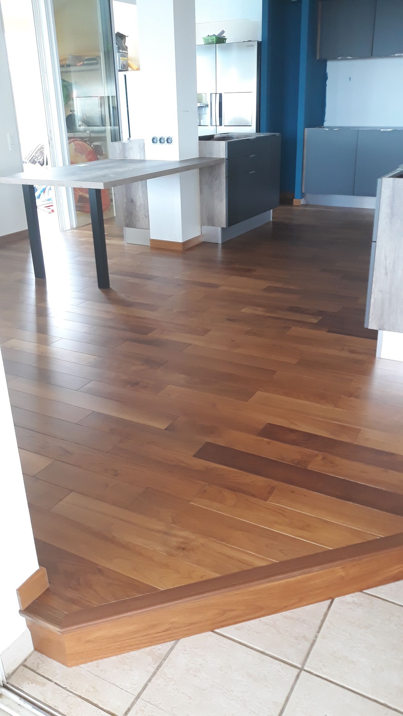 Sol en bois avec une petite marche menant à une pièce moderne aux murs bleus et aux tables blanches.