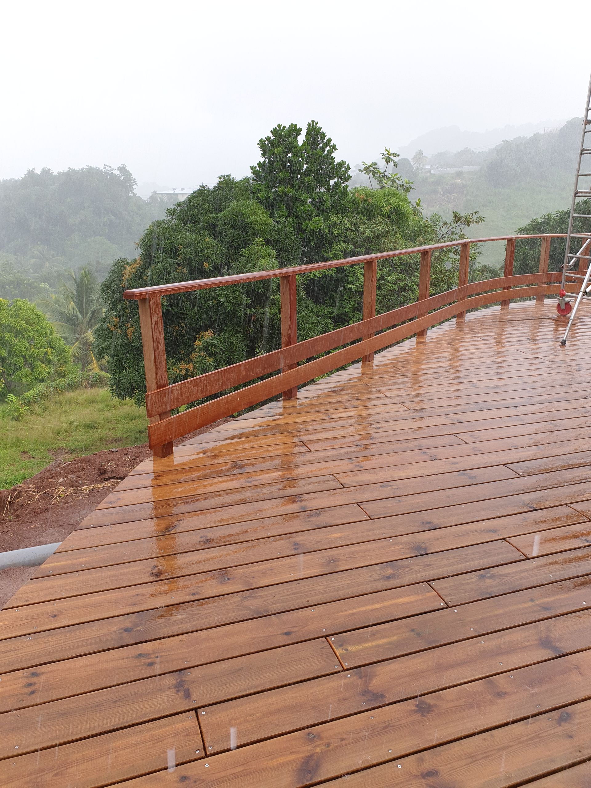 Terrasse en bois sous la pluie, surplombant des collines verdoyantes et des arbres dans la brume