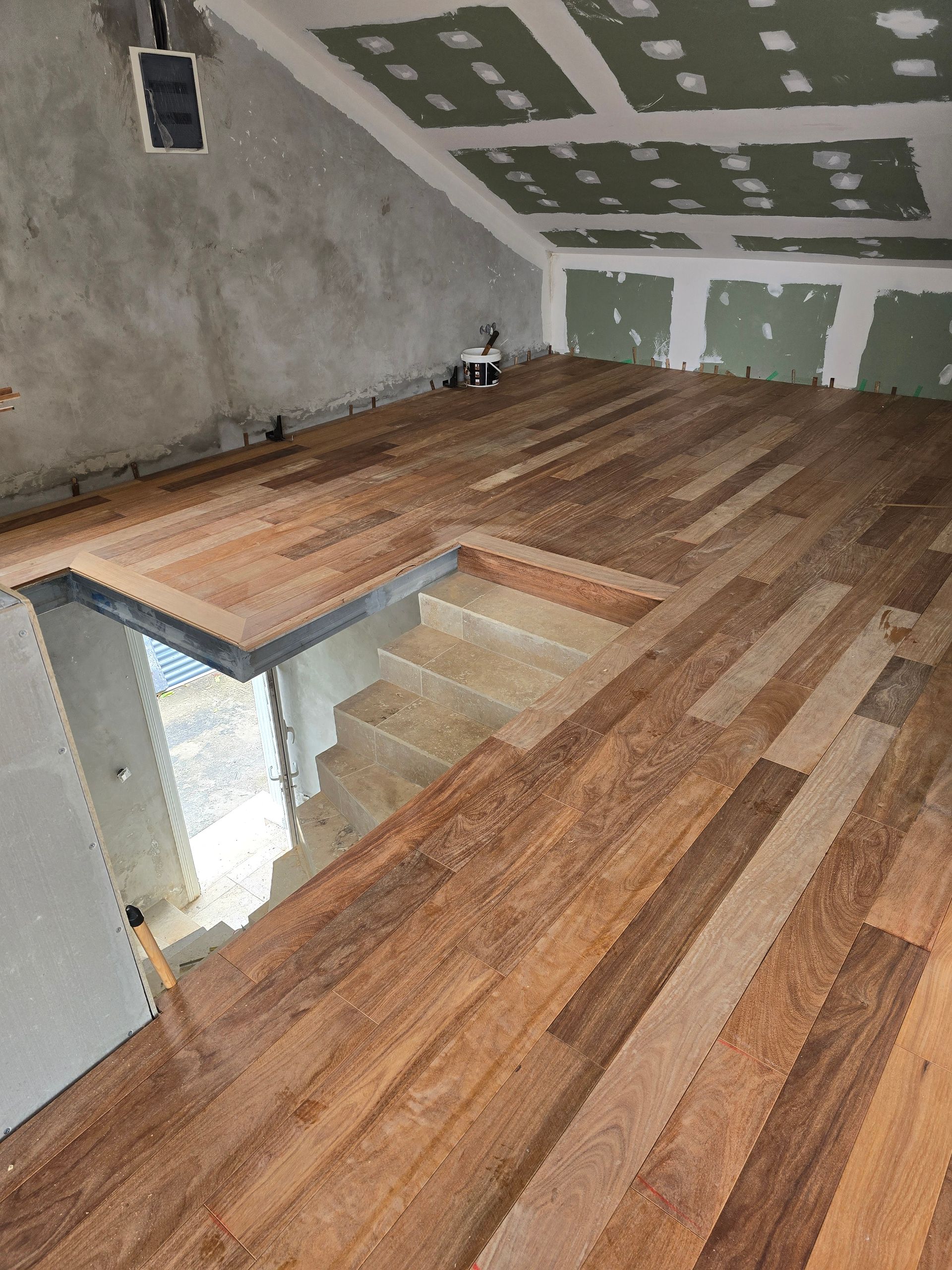 Pièce de grenier inachevée avec un plancher en bois, un plafond mansardé et une ouverture pour l’escalier.