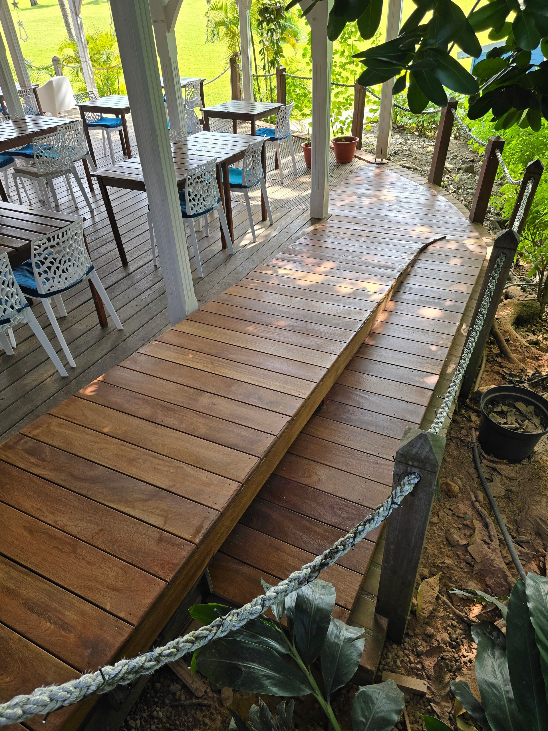 Rampe en bois avec des mains courantes menant à une terrasse extérieure et à des tables sous les arbres