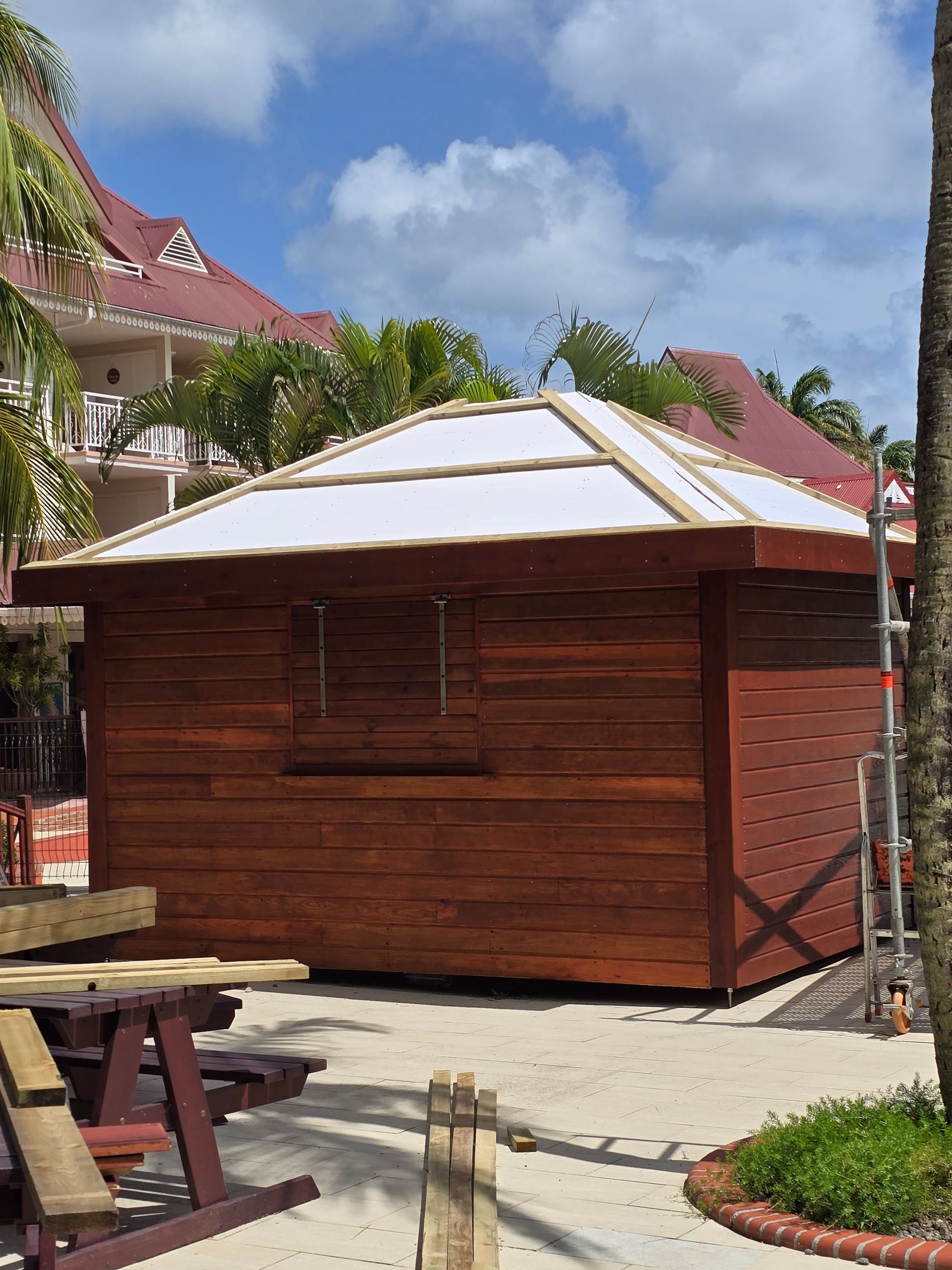 Kiosque en bois au toit blanc dans un parc ensoleillé, avec des tables de pique-nique à proximité.