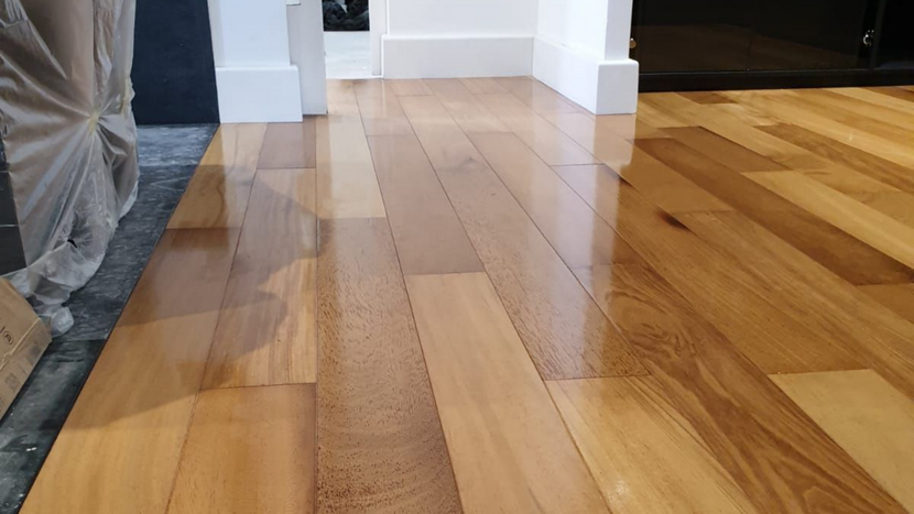 Parquet en bois poli dans une embrasure de porte, avec la lumière qui se reflète sur la surface et un objet recouvert de gris à gauche