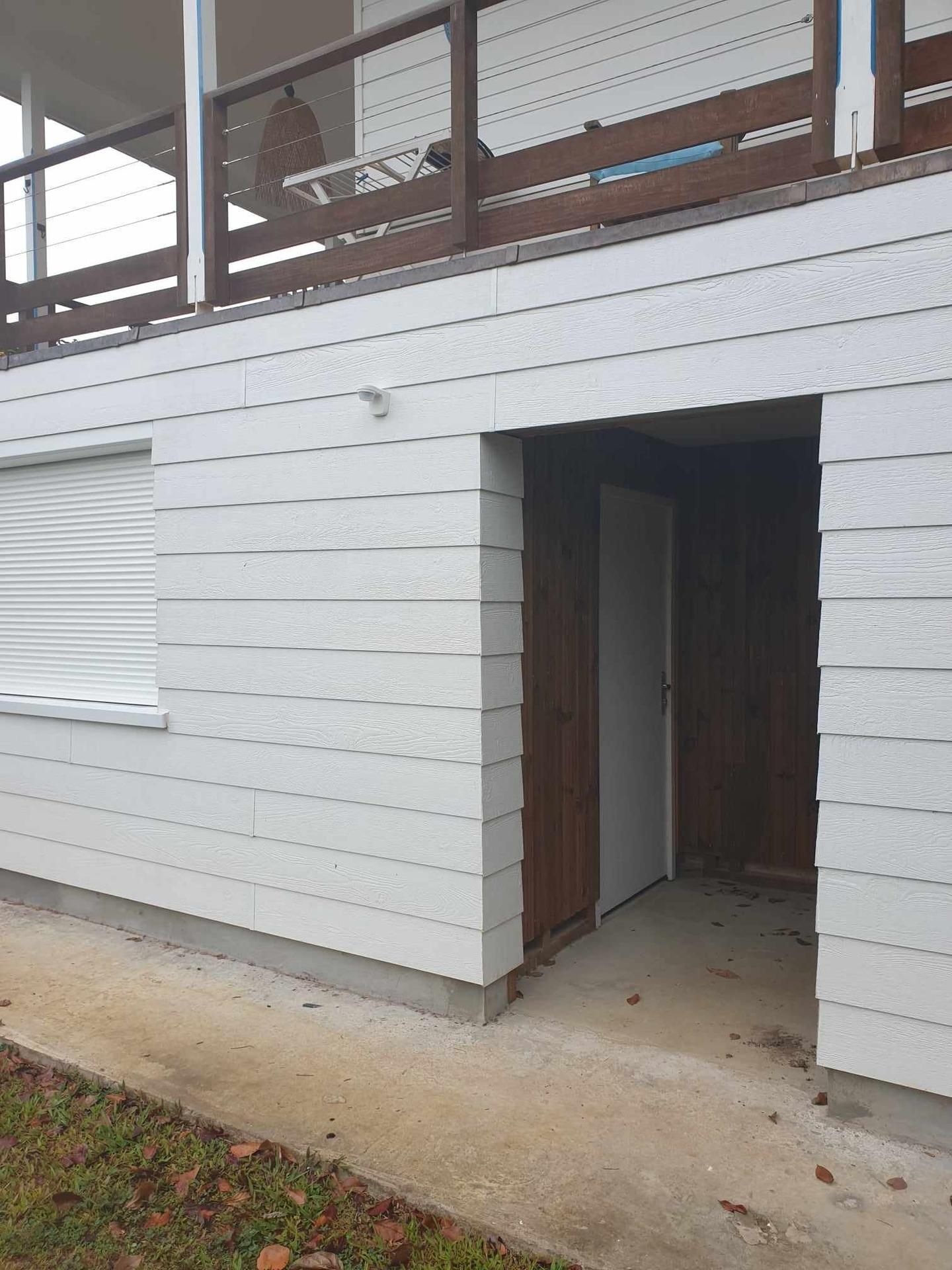 Façade blanche avec une porte ouverte et un balcon en bois au-dessus, vue de l’extérieur