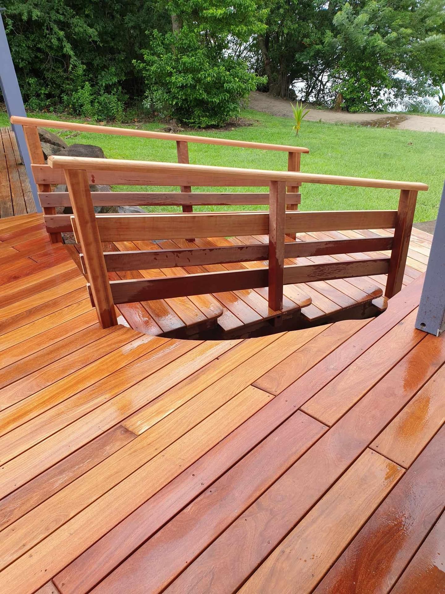 Terrasse en bois avec un petit escalier et une rampe menant à un jardin gazonné