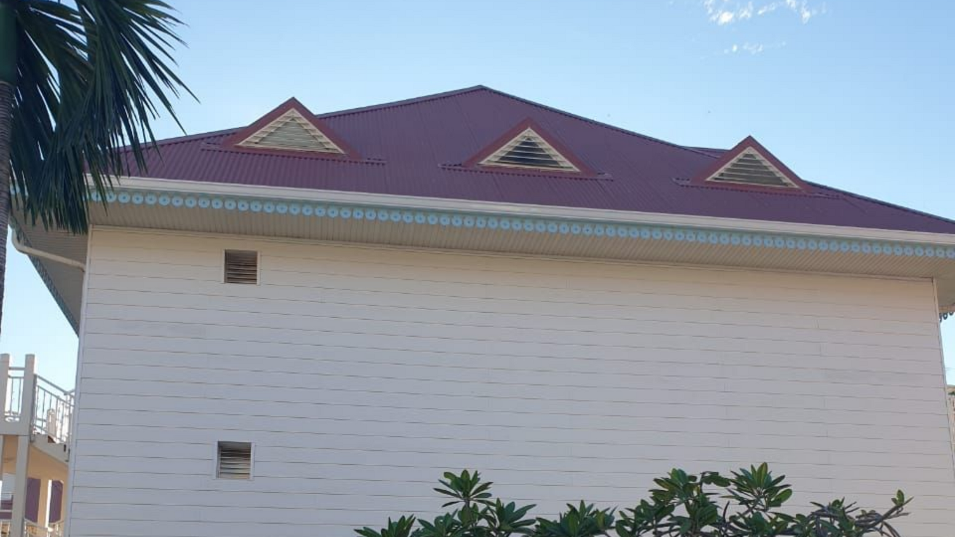 Bâtiment blanc avec un toit rouge et trois petites fenêtres triangulaires sous un ciel bleu.