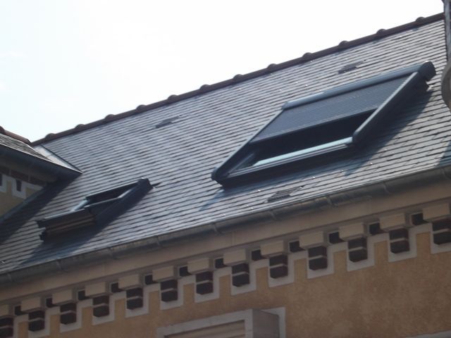 Toiture en ardoise avec deux puits de lumière sur un bâtiment beige, sous un ciel couvert