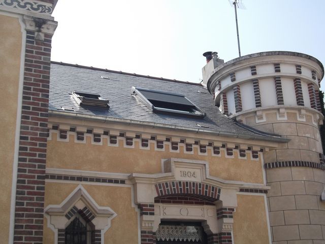 Bâtiment historique en briques avec un toit gris et une tour ronde en pierre sous un ciel lumineux
