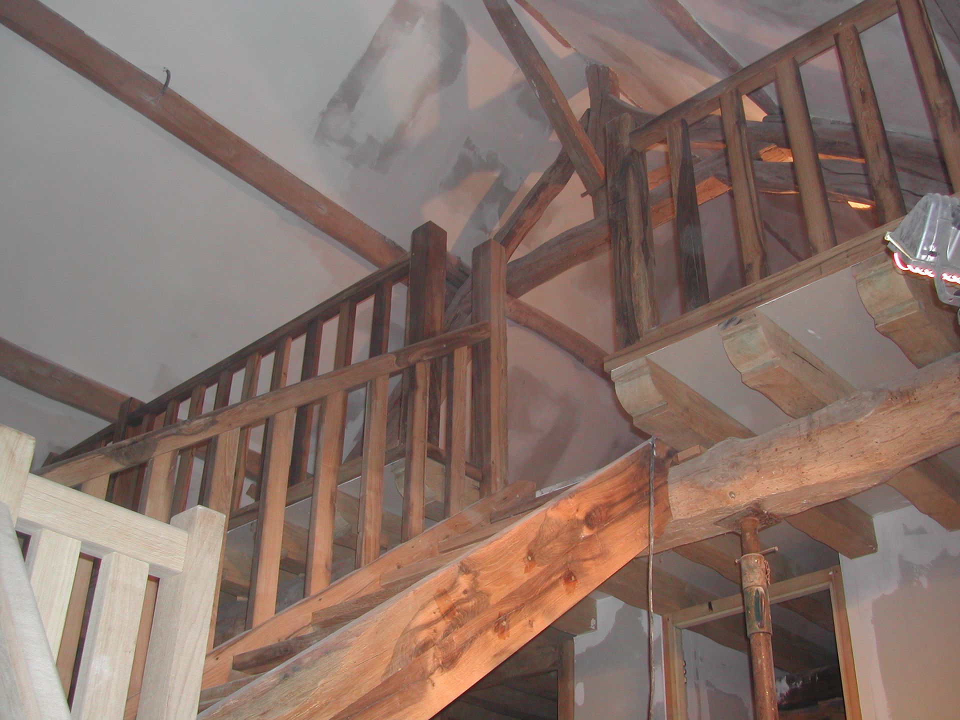 Escalier et rampe en bois à l’intérieur d’une maison, avec des dégâts causés par la fumée et des poutres de plafond calcinées au-dessus.