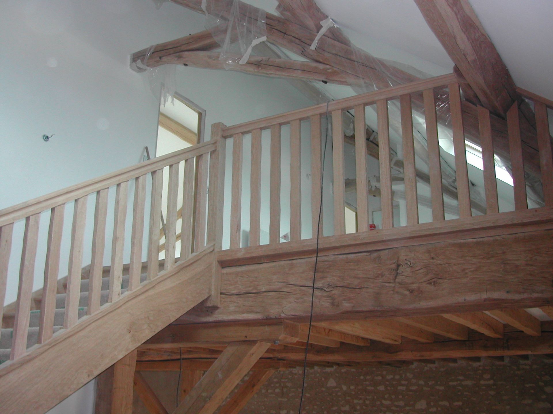 Garde-corps en bois et escalier dans un grenier en cours d’aménagement, avec poutres apparentes et murs bleu clair