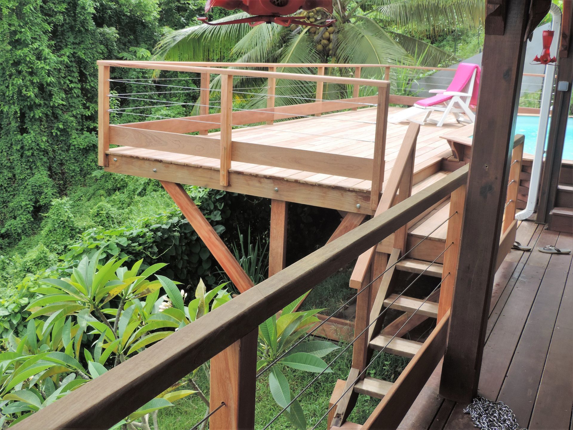 Balcon en bois avec garde-corps et escalier donnant sur une végétation luxuriante