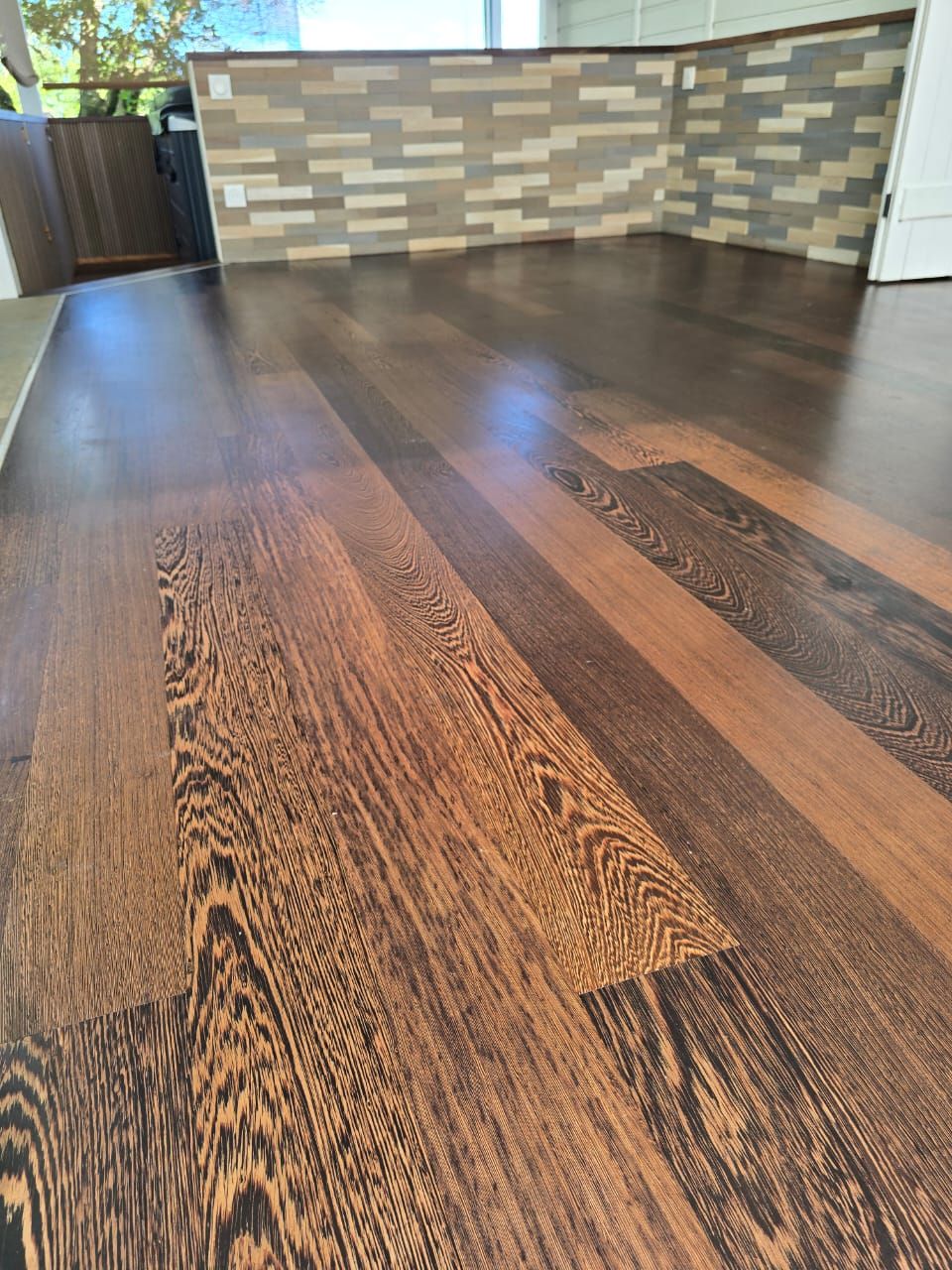 Gros plan sur un parquet en bois poli au grain foncé, avec un mur carrelé incurvé en arrière-plan